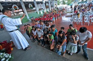  blessing. Fr. Anthony Morello blesses the Yolanda survivors from Eastern Visayas who sought refuge at the barangay Tinago gym last year and settled here in Metro Cebu. (CDN PHOTO/ JUNJIE MENDOZA)