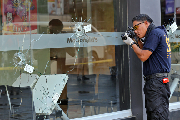 SHATTERED. A forensics technician marks and documents the bullet holes in the glass panel of the McDonald’s  outlet in barangay Tabunok in Talisay City. CDN PHOTO/JUNJIE MENDOZA