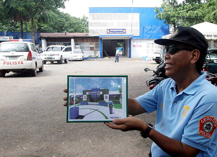 A policeman shows an illustration of how the  new Cebu City Police Office would look after the dilapidated building behind him is renovated.  (CDN FILE PHOTO)