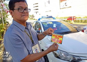 Reynaldo Elnar, OIC of the LTFRB- 7, shows the sticker placed on taxis advising the public to deduct P10 from the meter fare in order to implement the nationwide rollback of the flag down rate. (CDN PHOTO/LITO TECSON)