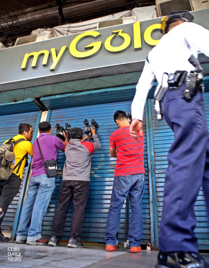 TV cameramen try to take a footage through a hole in the metal roll-up door of My Gold store after a Saturday morning heist.