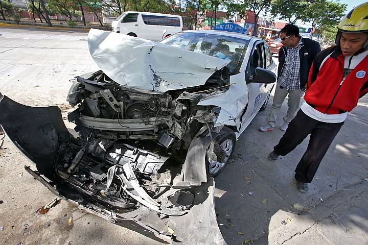 Bystanders look at the severely damaged taxi driven by Valerio Boybanting at the S. Osmeña Road in front of the Cebu Daily News building. The taxi was hit by an oncoming SUV on Thursday evening. (CDN Photo/Junjie Mendoza)