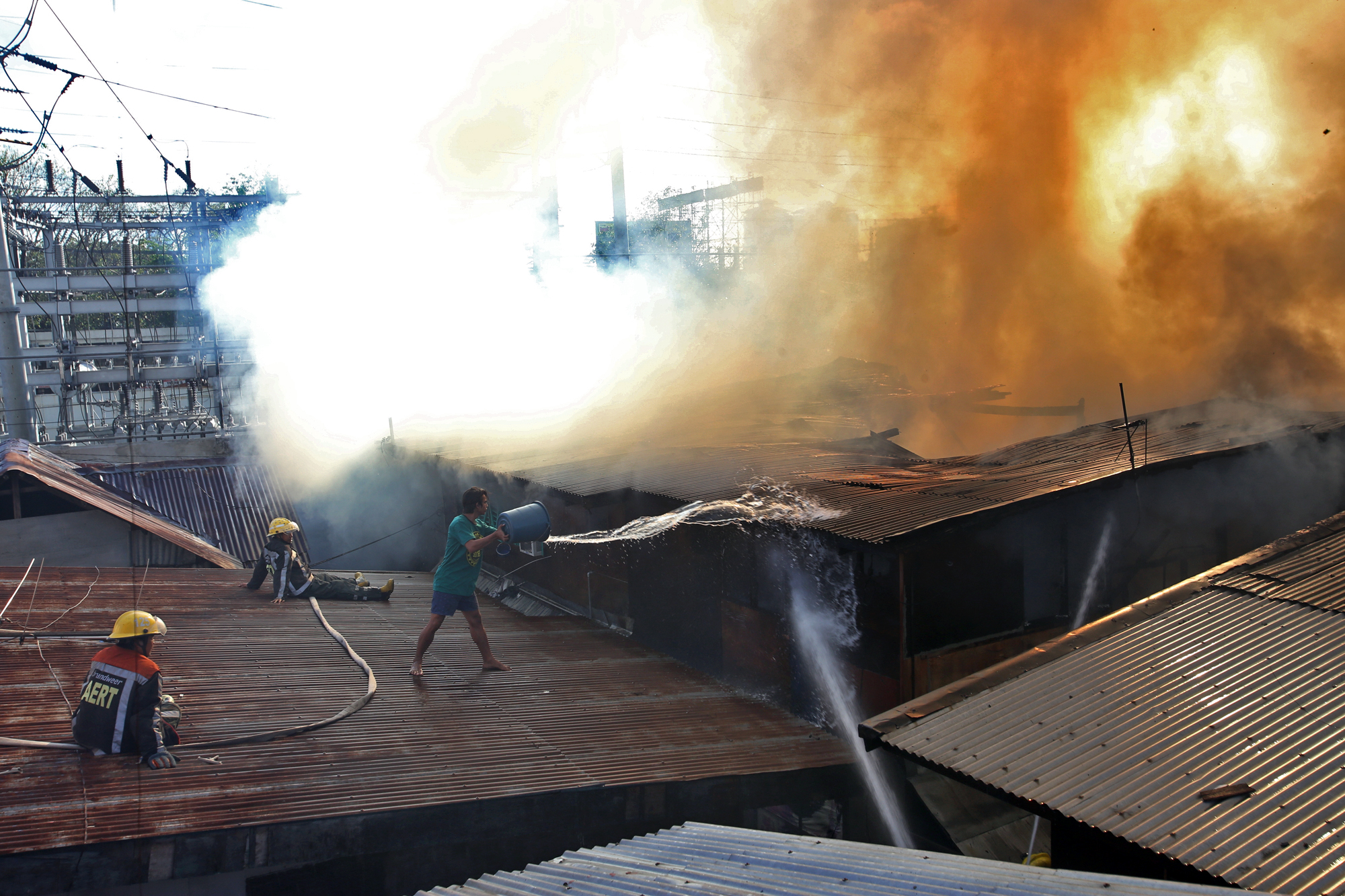 A resident of barangay Lorega San Miguel throws a pail of water on a burning house while fire volunteers sit on the roof waiting for water pressure.(CDN/JUNJIE MENDOZA)