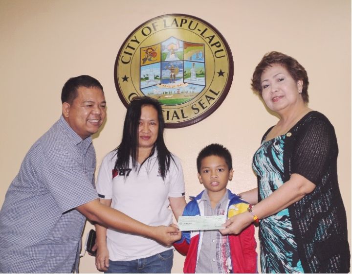 Mayor Paz Radaza turns over the check worth P 125,000 to Jerish John Velarde (second from right), along with his parents, at the mayor's office.(Contributed)