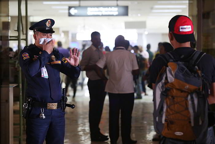 A security officer of the Mactan-Cebu International Airport (MCIA) covers his nose with a handkerchief  to protect himself from smoke as he stops a passenger from entering the international arrival area, which had to be evacuated as  smoke from a busted air handling unit filled the site. (CDN PHOTO/ JUNJIE MENDOZA)