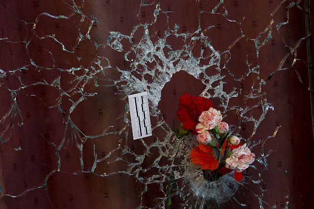 Flowers are placed in a window shattered by a bullet as people pay their respects to the victims of the attacks on Le Petit Cambodge (Little Cambodia)restaurant and the Carillon Hotel during the first of three days of national mourning in Paris. (AP Photo)