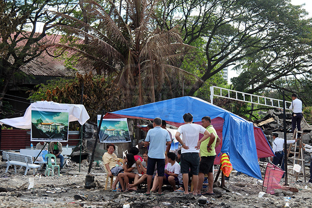 Lahug fire victims put up tents at the fire site where their destroyed houses once stood as UP guards (right, climbing ladder) installs tarp banners of images of UP building to be constructed on the lot. (CDN PHOTO/TONEE DESPOJO)