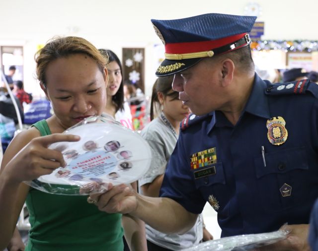 Supt. Renato Dugan, Regional Police Community Relations officer (PCR), distributes fans printed with photos of the 10 most wanted persons in Central Visayas. (CDN PHOTO/JUNJIE MENDOZA)