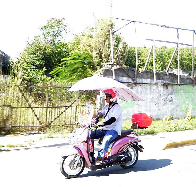 A man finds a novel way to drive on a motorcycle on a hot day -- adding an umbrella as an accessory to his motorcycle. | CDN file photo