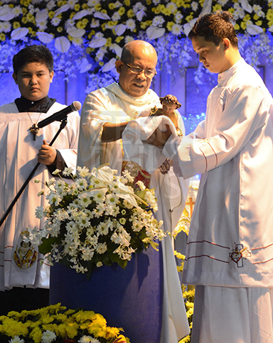 Fr. Jonas Mejares (center), who celebrated the Mass, wipes the image with a towel after dipping it in water. (CDN PHOTO/CHRISTIAN MANINGO)