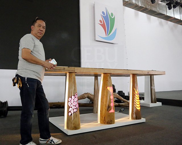 Cebu furniture designer Clayton Tugonon used wood from storm-damaged boats and houses to make the altar table for the IEC Pavilion. On the front legs, images of a chalice, grapes for wine, and wheat for bread are backlighted with LED units. (CDN PHOTO/JUNJIE MENDOZA)