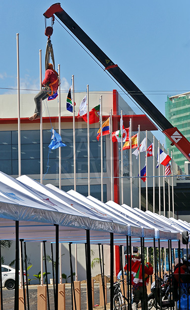 A construction worker dangles from a crane as he sets up the flags of participating nations outside the IEC Pavilion in barangay Mabolo, Cebu City. (CDN PHOTO/JUNJIE MENDOZA)