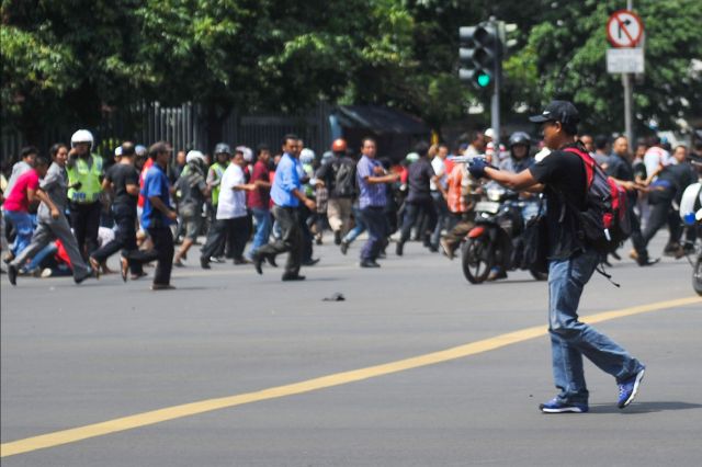 An armed man walks on Thamrin Street near Sarinah shopping mall in Jakarta, Indonesia as people scamper for safety in this photo released by China’s Xinhua News Agency. (AP PHOTO)