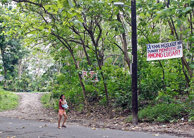 A girl carrying her baby passes by the signages put up by residents of Barangay Kalunasan who opposed plans to build a cemetery at the Osmeña Shrine in this 2011 file photo.