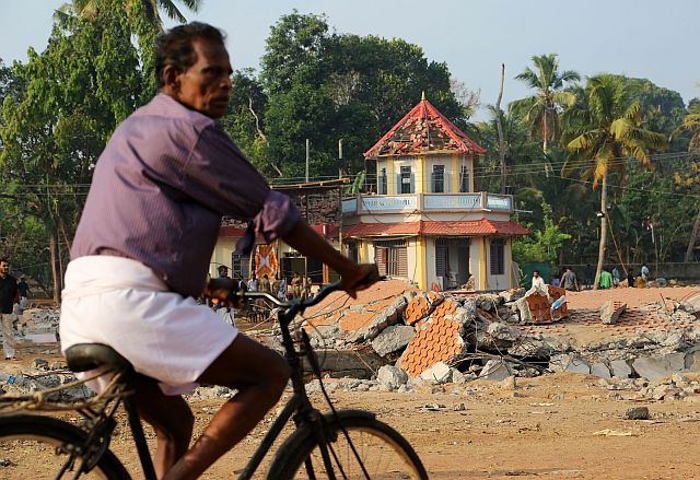 A cyclist rides past damaged structures at the spot where a massive fire broke out during a fireworks display at the Puttingal temple complex in India. (AP)