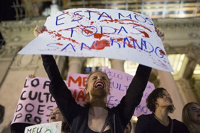 A woman shouts holding a banner that reads in Portuguese “We’re all bleeding” as she protests the gang-rape of a 16-year-old girl in Rio de Janeiro, Brazil on Friday./AP
