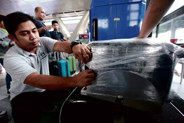Travelers have their luggage wrapped in plastic for P160 a piece as security against the “tanim bala” racket at Ninoy Aquino International Airport. (INQUIRER)