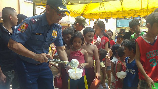 From guns to ladle. Doing away from his duty as a police officer, Supt. Michael Bastes conducts feeding program among street children and kids in Barangay Day-as in Cebu City last Sunday. (CDN PHOTO APPLE MAE TA-AS)