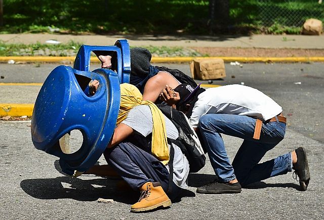Students take cover from tear gas and rubber bullets fired by police during a demonstration by students from the Central University of Venezuela demanding a referendum on removing President Nicolas Maduro. (AFP)