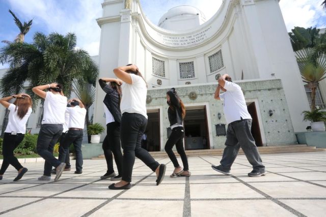 Capitol employees cover their heads while going towards the safe area outside of the Capitol building during Tuesday morning's surprise earthquake drill. (CDN PHOTO/LITO TECSON)