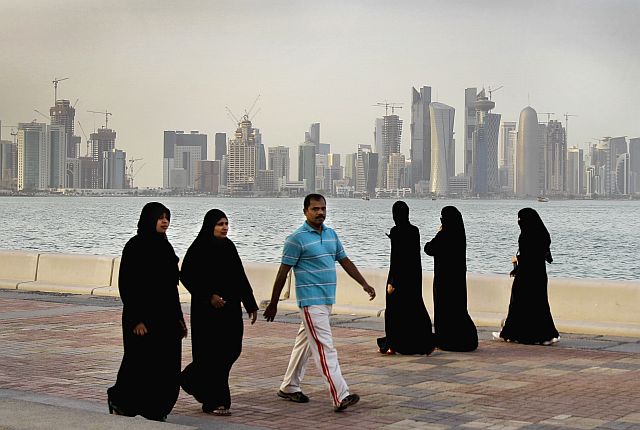 Qatari women and a man walk by the sea with the new high-rise buildings of downtown Doha in the background in this April 7, 2012 file photo. The economic slowdown gripping countries across the Persian Gulf can be seen in layoffs, slowed construction projects and government cutbacks. (AP)