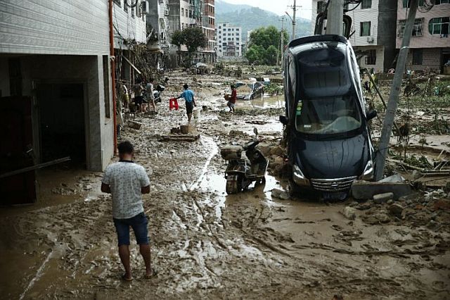 Residents walk past a damaged car in the aftermath of a tropical storm in Bandong town, China’s Fujian province. AFP