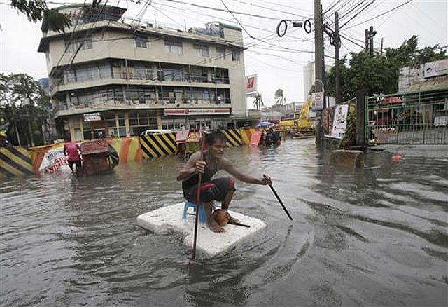 A man uses sticks to move a styrofoam block he is riding along a flooded road in suburban Mandaluyong, east of Manila. /AP