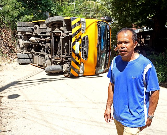 The East Visayan Academy bus lies on its side after the accident along a steep stretch in Barangay Pit-os while bus driver Eduardo Cagas stands nearby. ( CDN PHOTO/ LITO TECSON)