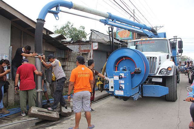 Clean up participants use the suction hose connected to a truck to pull the clog through the drain opening in Barangay Basak, Lapu-Lapu City. (CDN PHOTO/NORMAN MENDOZA)
