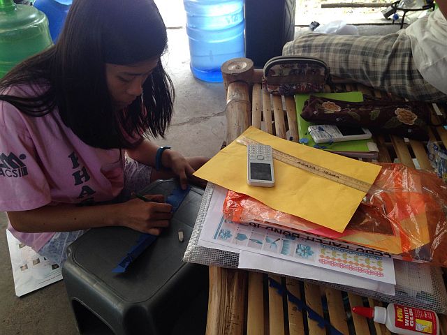 Angel Mae Lazaga, Grade 11 student makes her math project inside their makeshift house at the CICC grounds.  (CDN PHOTO/JULIT JAINAR)