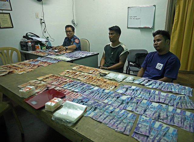 Guadalupe Police Chief, Chief Insp. Jose Gesto, shows the packs of shabu and money confiscated from drug suspects Richard Balucam (center) and Junryl Bulat-ag (right) in separate operations in Sitio Lareha, Barangay Kalunasan, and in 4th Street Guadalajara, Barangay Guadalupe. (CDN PHOTO/LITO TECSON)