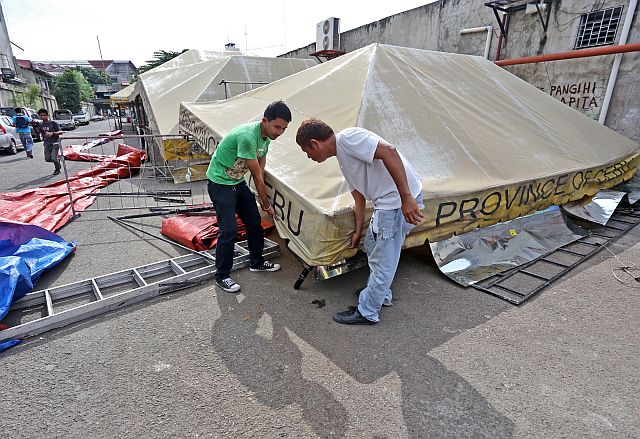 A sudden strong blast of wind topples down tents and chairs at the South Bus Terminal yesterday afternoon; while laborer Franklin Canoy Jr.  (right) and maintenance worker  Philip Salve Tañeza were blown away by the wind in a freak accident.  Both are shown here trying to fix the tents. (CDN PHOTO/JUNJIE MENDOZA)