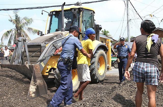 A police officer stops a fire victim from blocking a bulldozer at the fire site in this June 3, 2016 file photo.