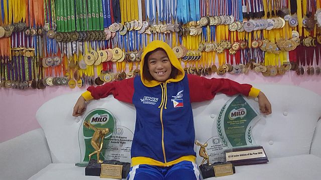 Kyla Soguilon proudly shows her Milo plaques and a wall filled with medals at her home in Kalibo, Aklan.  (Contributed photo by Kokoy Soguilon)
