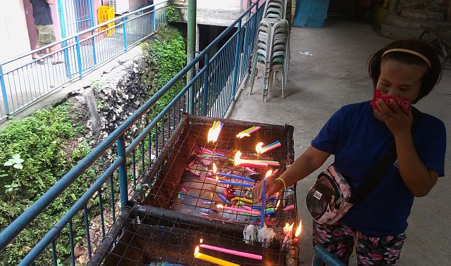 The foul odor coming from the Kalunasan Creek prompts a devotee of the Our Lady of Guadalupe de Cebu to cover her nose while offering candles and petitions at the Langub Shrine to avoid the dizzying stench.  (CDN PHOTO/TONEE DESPOJO)