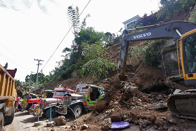 A backhoe operator started clearing the road of soil that buried the vehicles, including one car in the area. (CDN PHOTO/JUNJIE MENDOZA)