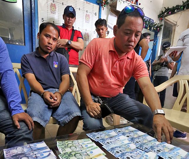 Junrey Cagay, 28, (left in handcuffs) of Barangay Quiot, Cebu City, is being questioned  by Councilor Dave Tumulak (right) after the man was arrested for manufacturing fake money bills (on the table) inside an internet café in Colon Street. (CDN PHOTO/JUNJIE MENDOZA)