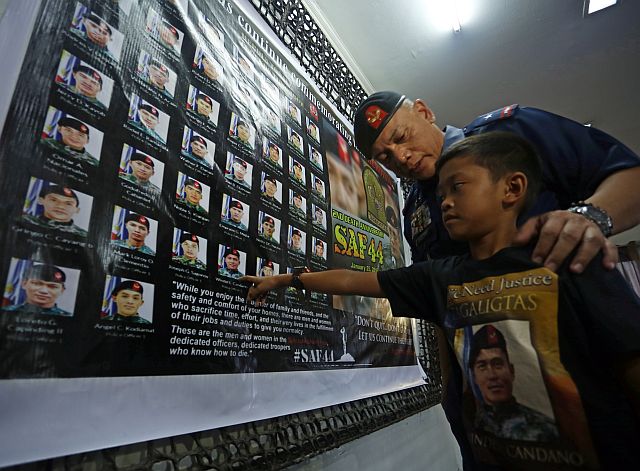 Chief Supt. Noli Taliño, Police Regional Office chief, accompanies Sian Gabriel Candano, son of slain PO1 Windel Candano, as he points to a photo of his father in the list of 44 Special Action Force (SAF) commandos during the second year commemoration of the tragedy at the PRO-7 Chapel. (CDN PHOTO/LITO TECSON)