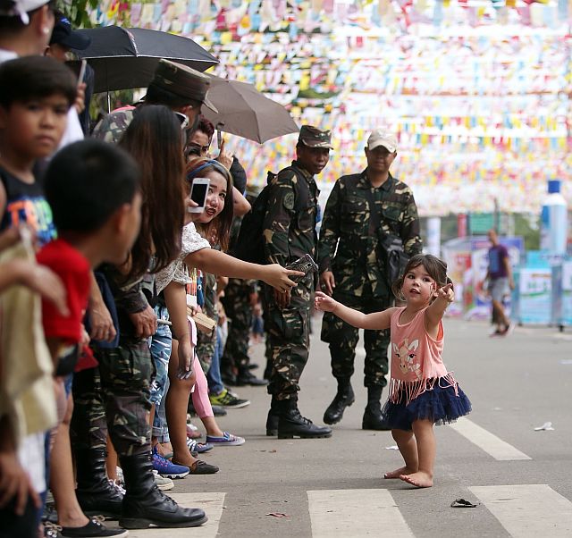 A little girl grabs a hand while pointing toward the Sinulog dancers (CDN PHOTO/LITO TECSON)