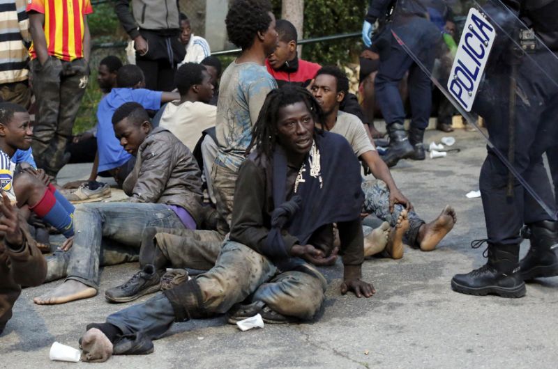 Migrants sit on the ground next to Spanish police officers after storming a fence to enter the Spanish enclave of Ceuta, Spain, Friday.  /AP