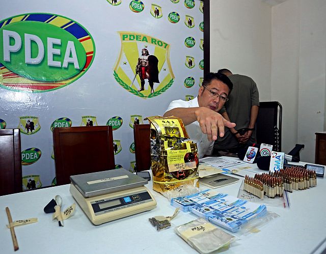 PDEA-7 Director Yogi Filemon Ruiz shows the items confiscated from alleged big-time drug dealer Rogelio Romo, a resident of Barangay Agus, Lapu-Lapu City. One kilo of shabu, valued at P6 million, was kept by Romo inside a Chinese tea package. Drug dealers have resorted to several ways to avoid detection. Romo is shown here with his back to the camera. (CDN PHOTO/LITO TECSON)