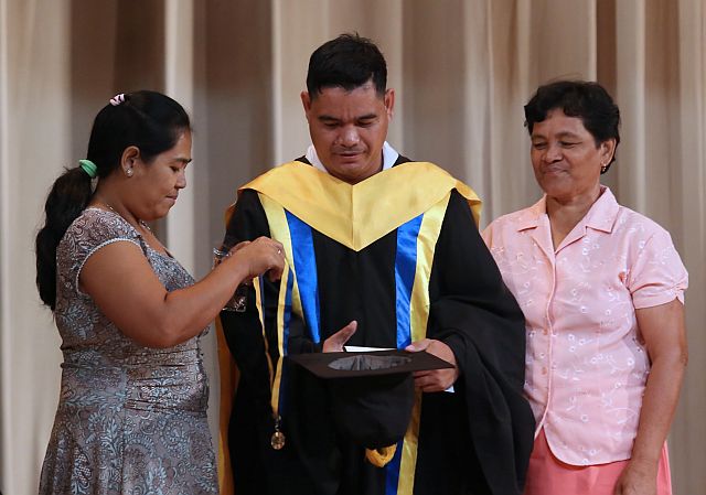 Irenea Macua (left), with her mother-in-law Aproniana Macua looking on, prepares to put on the cum laude medal on her husband Erwin, who earned his Bachelor of Elementary Education degree at Saint Theresa’s College while working as the school’s security guard. (CDN PHOTO/JUNJIE MENDOZA)