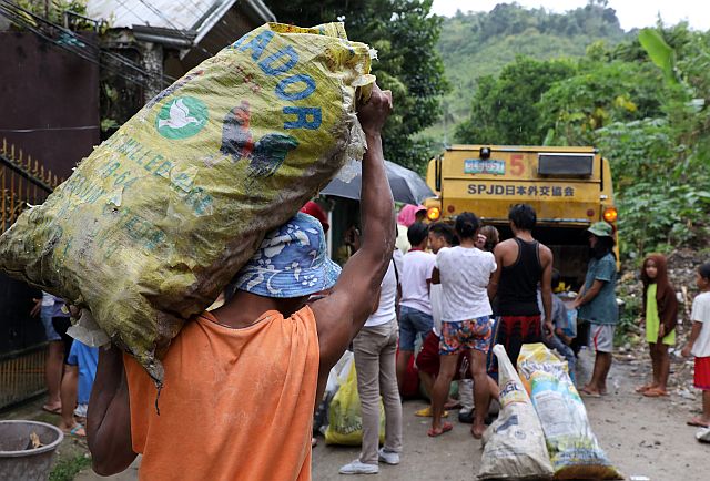  Residents from Cebu City’s interior sitios or zones  rush to load the bags of trash they collected into a compactor truck to be able to claim the cans of sardines the city is giving away in exchange for their garbage. (CDN PHOTO/TONEE DESPOJO)