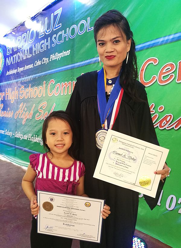 Carmel A. Deloy, a former househelp, poses with her five-year-old daughter, Stephanie, as they proudly show off her certificates after graduating, with honors, at the Barrio Luz National High School. Carmel is among the first to finish grade 12 in Cebu City’s K-12 pilot schools.  CDN PHOTO/CHRISTIAN MANINGO