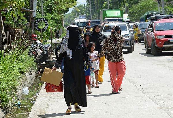 Residents fleeing from Marawi, where gunmen who had declared allegiance to the Islamic State group rampaged through the southern city, walk past a checkpoint at the entrance to Iligan on the southern Philippine island of Mindanao on May 24, 2017. Philippine President Rodrigo Duterte warned on May 24 that martial law would be "harsh" and like a dictatorship, after imposing military rule in the south of the country to combat Islamist militants. / AFP PHOTO / TED ALJIBE