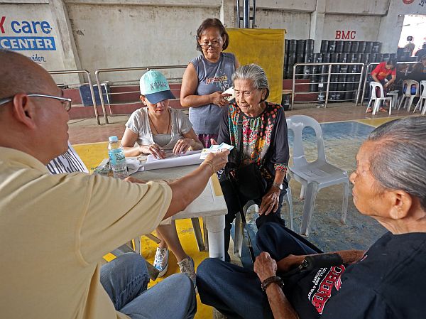 Benigna Yares and her husband Agustin Yares (seated at right), both in their 90s, receive their senior citizen cash aid at the Mabolo Sports Center. (CDN PHOTO/LITO TECSON)