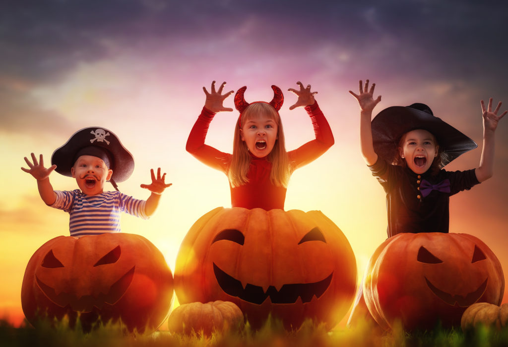 Cebu Catholic Church discourages ‘horror’ costumes, decorations, must wear saint attires instead. Happy brother and two sisters on Halloween. Funny kids in carnival costumes outdoors. Cheerful children and pumpkins on sunset background.