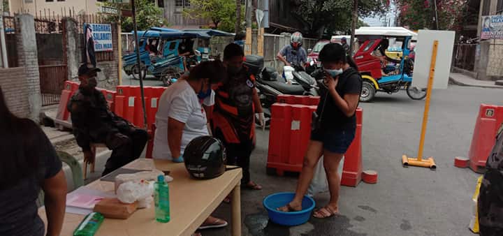 A resident of Burgos Street in Barangay Alang-Alang, Mandaue City, who are placed in home quarantine, go through the disinfection process at a station manned by police and health workers as the resident return from buying supplies for their families. | Norman V. Mendoza