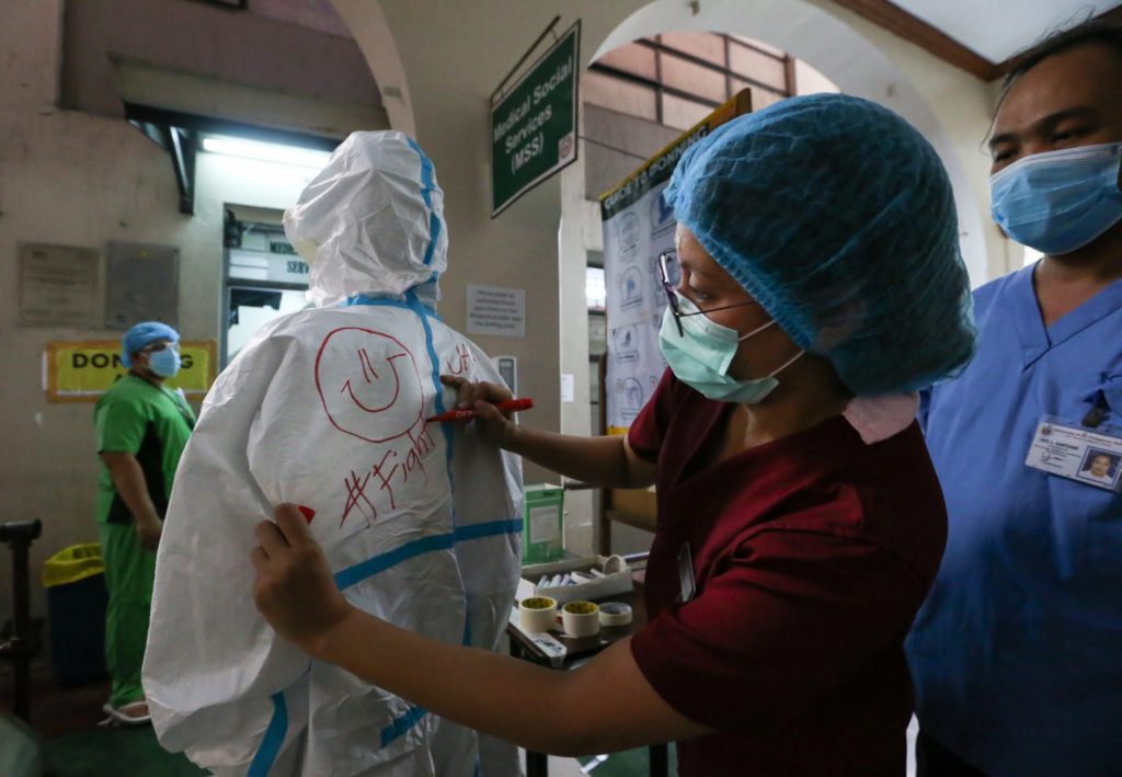 CHEERING NURSES UP. A nurse draws a smiley face on the back of a fellow health worker’s protective suit before she enters a COVID-19 ward at the Philippine General Hospital. | Inquirer photo