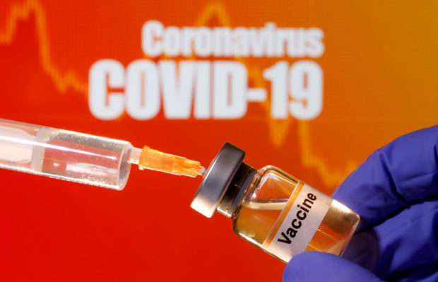 FILE PHOTO: A small bottle labeled with a "Vaccine" sticker is held near a medical syringe in front of displayed "Coronavirus COVID-19" words in this illustration taken April 10, 2020. REUTERS/Dado Ruvic